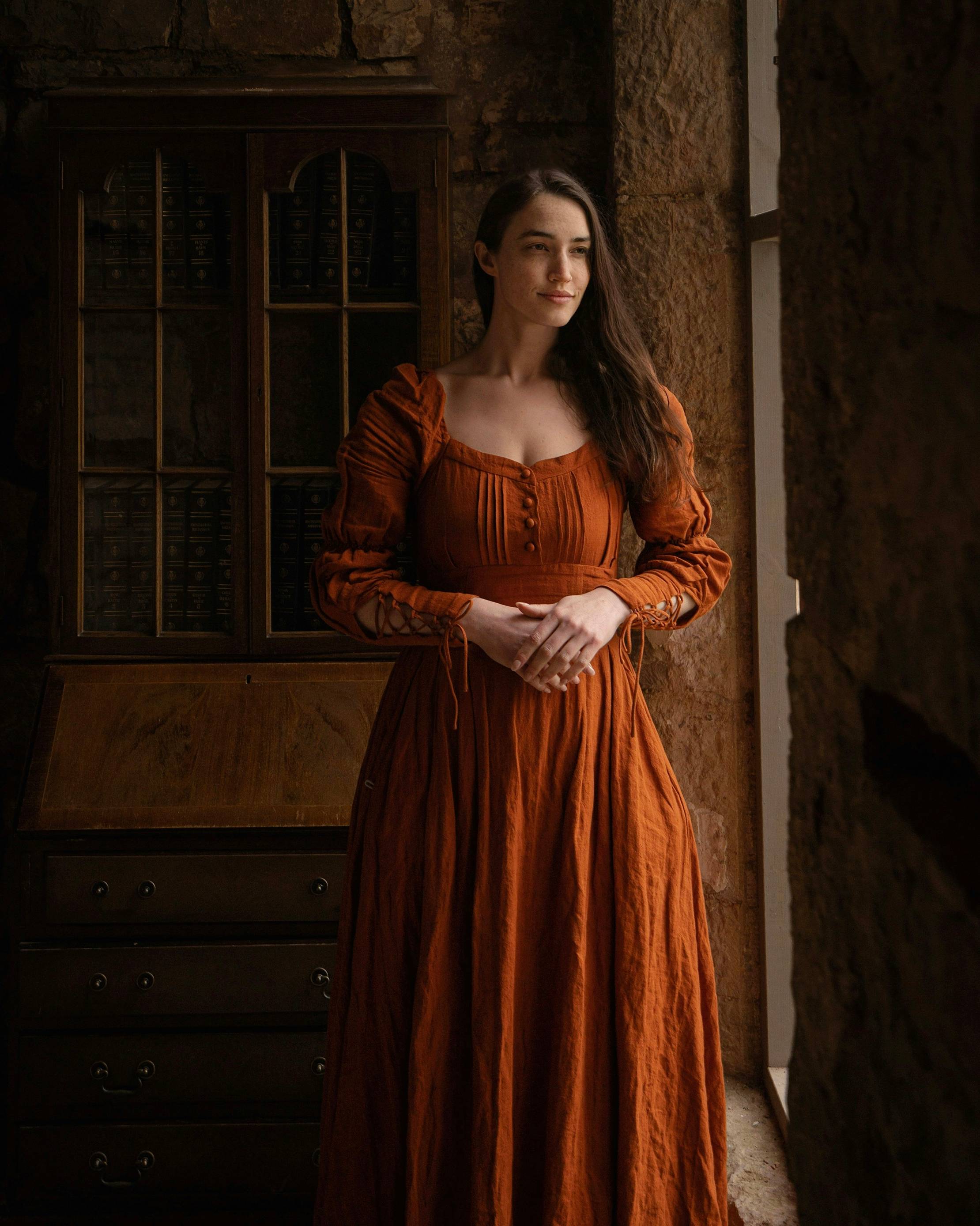 a woman in an orange dress standing by a window